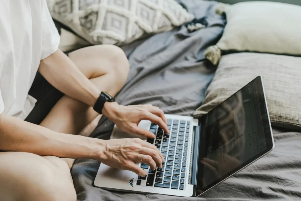 a person sitting on a bed using a laptop